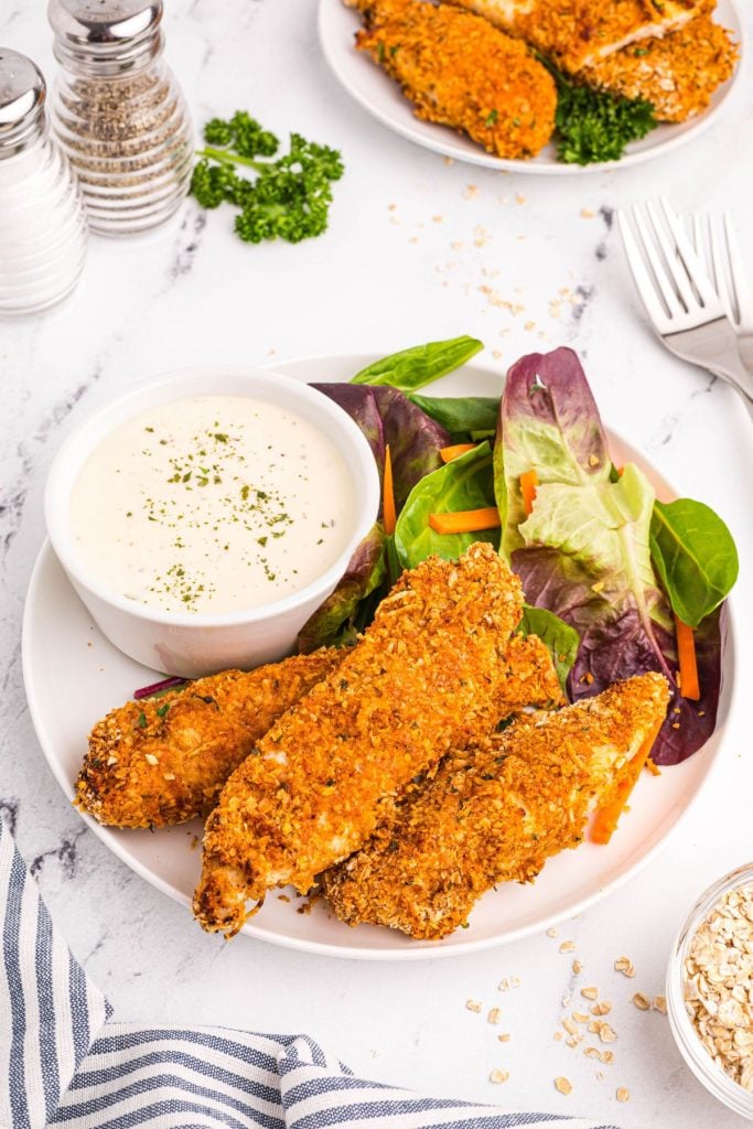 Golden oatmeal crusted chicken on a white plate with salad