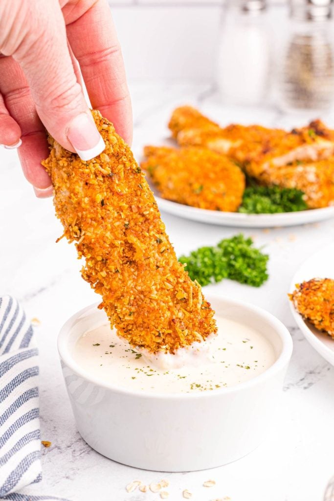 Oatmeal crusted chicken being dipped into ranch