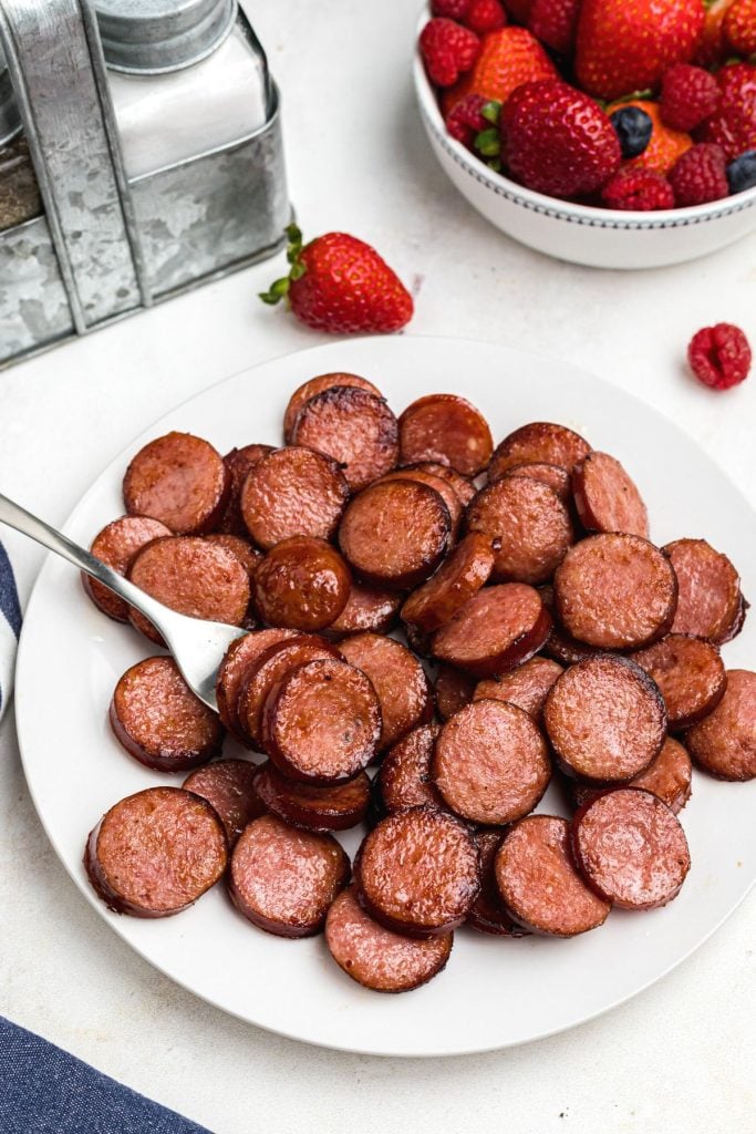 Juicy kielbasa slices on a white plate with fresh fruit on the table