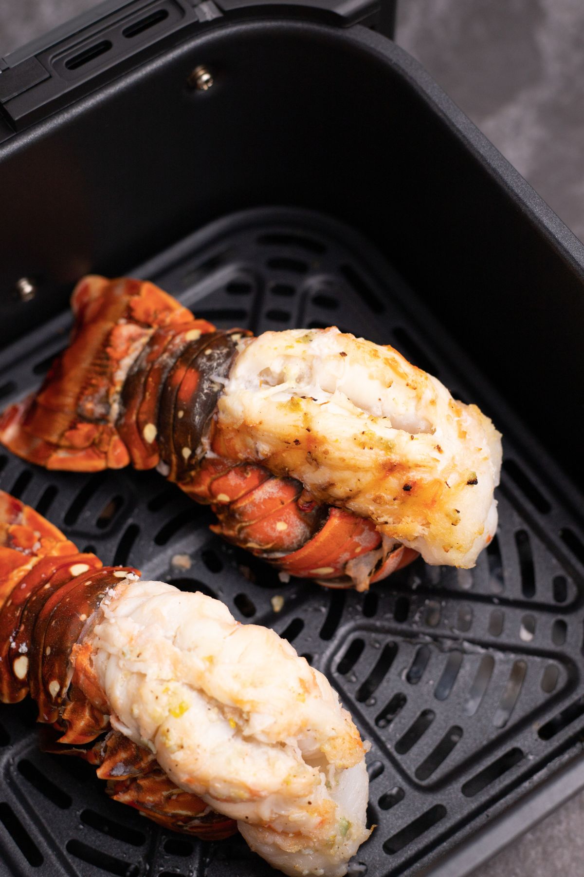Two red/orange lobster tails in the air fryer basket, after being cooked. 
