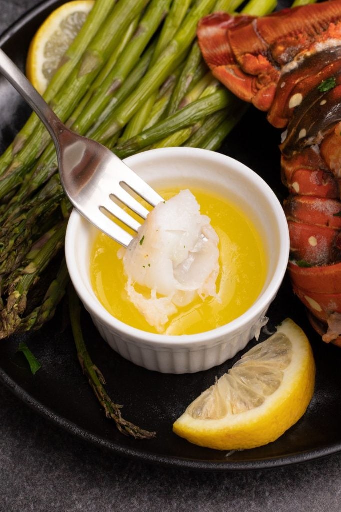 A fork dipping a piece of lobster meat into melted butter. 