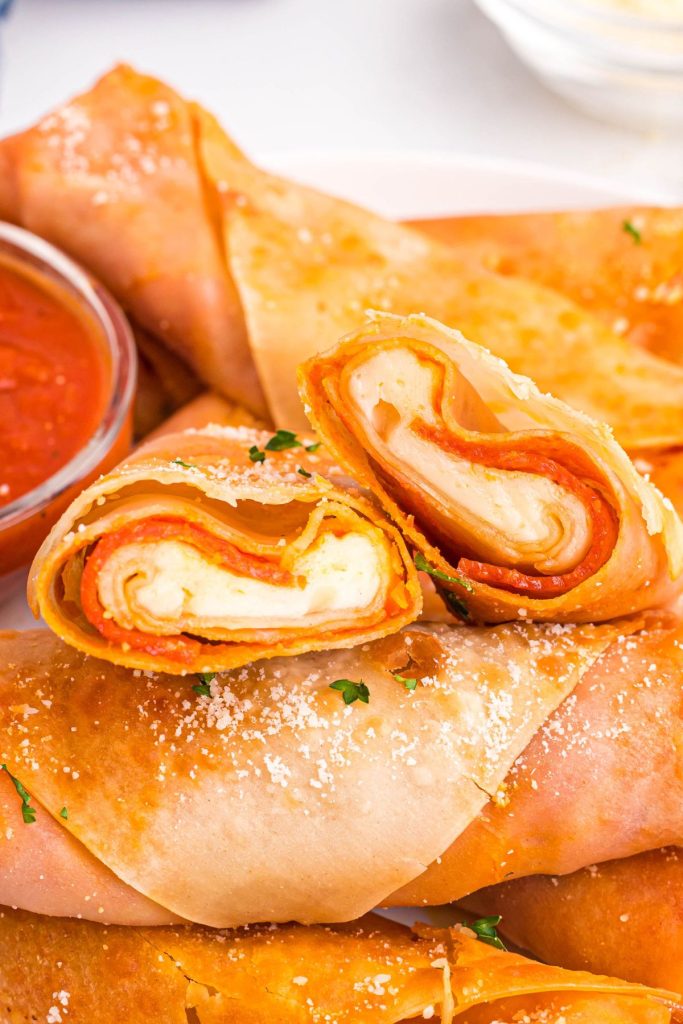 Golden crispy pizza egg rolls frilled with cheese and pepperoni stacked together. 