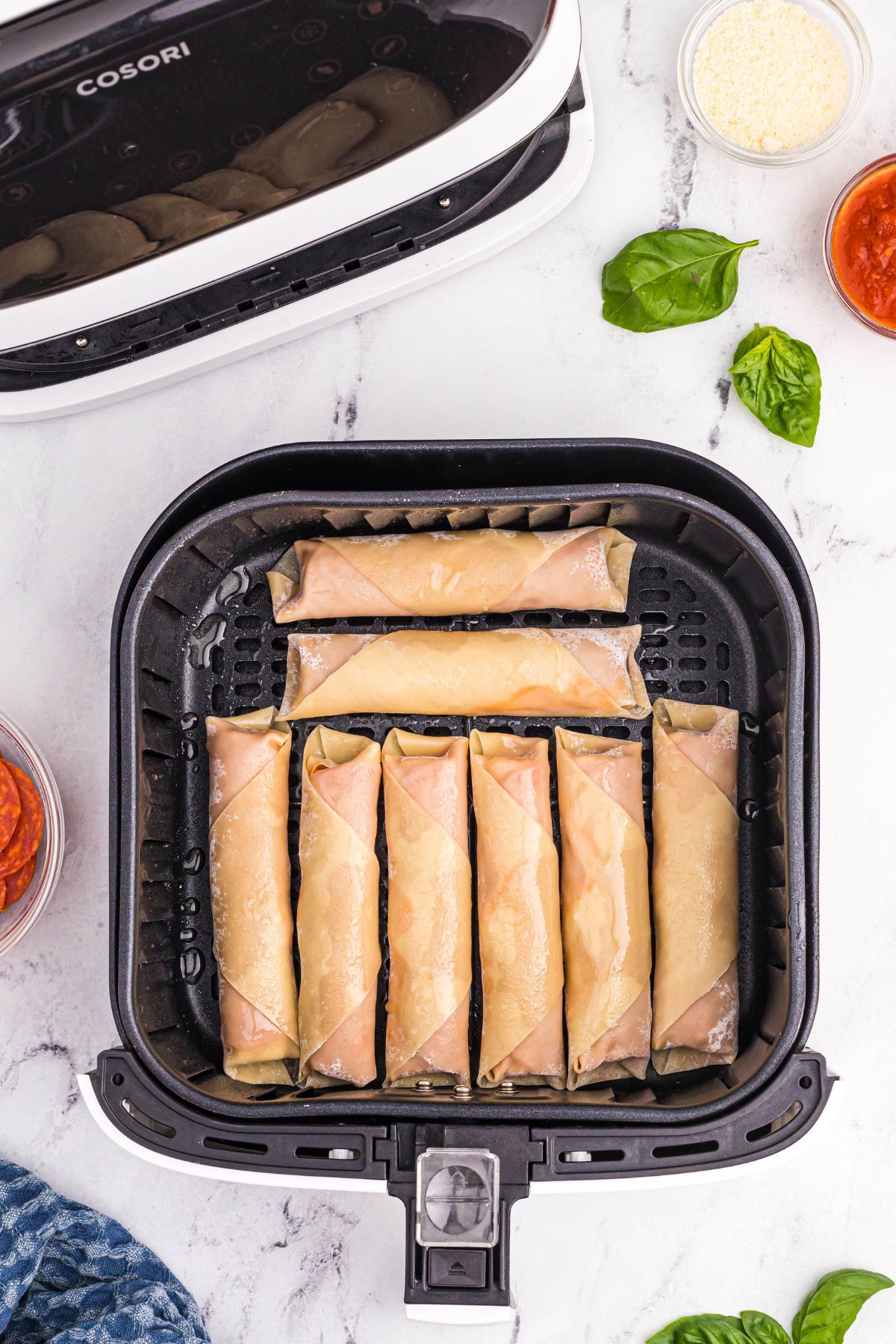 Uncooked rolled egg rolls in the air fryer basket