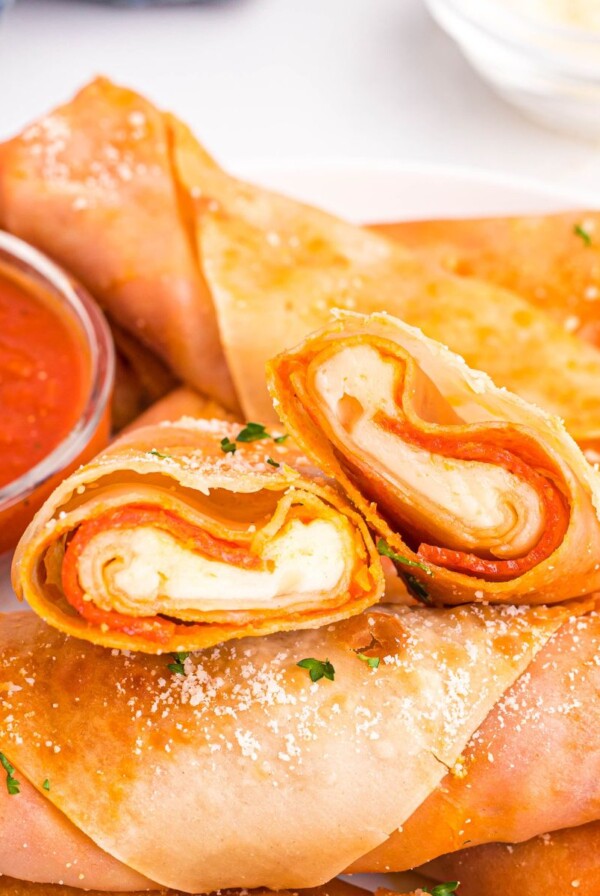 Golden crispy pizza egg rolls stacked on a white plate served with pizza sauce.