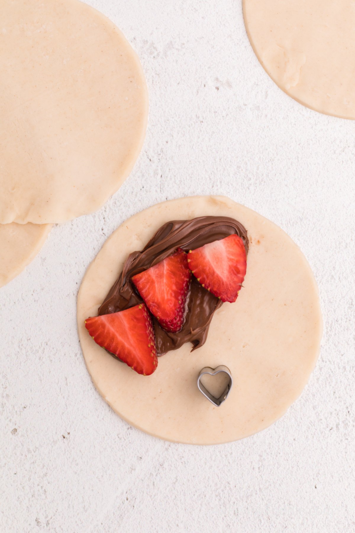 Nutella and strawberries on a sheet of dough with a small cutter for shapes.