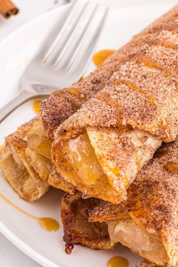 Golden crispy taquitos filled with apple pie filling on a white plate.