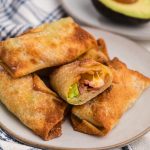 Air fryer avocado bacon egg rolls stacked on a plate with one missing a bite.