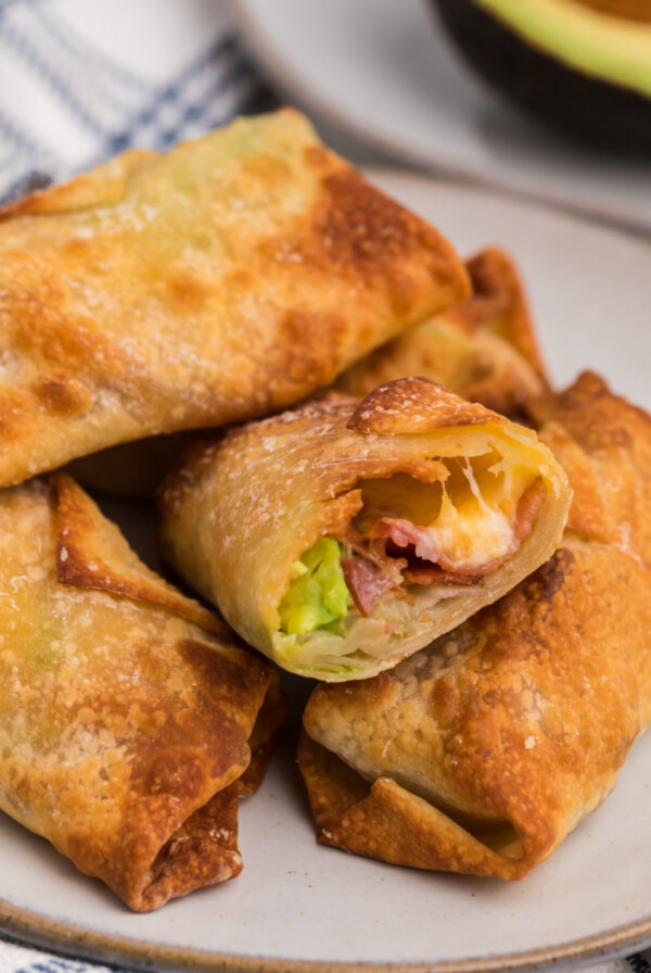 Air fryer avocado bacon egg rolls stacked on a plate with one missing a bite.