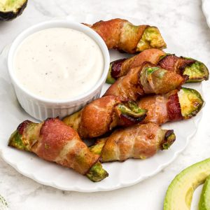 Crispy bacon wrapped around avocado wedges on a white plate
