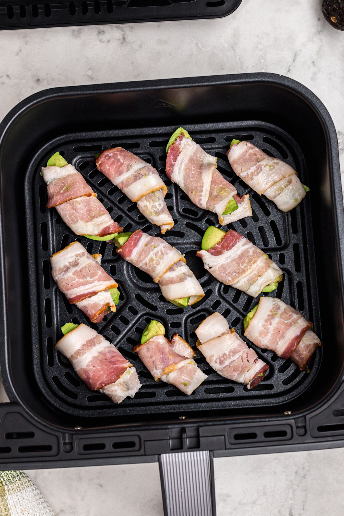Uncooked bacon slices wrapped around avocado wedges.