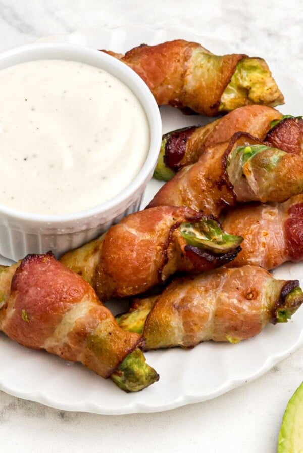 Crispy bacon wrapped around avocado wedges on a white plate