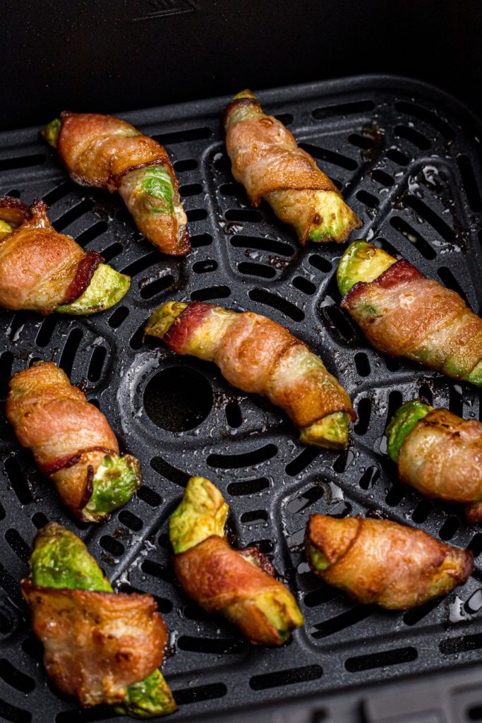 Crispy juicy bacon wrapped around avocado wedges in the air fryer basket after being cooked. 