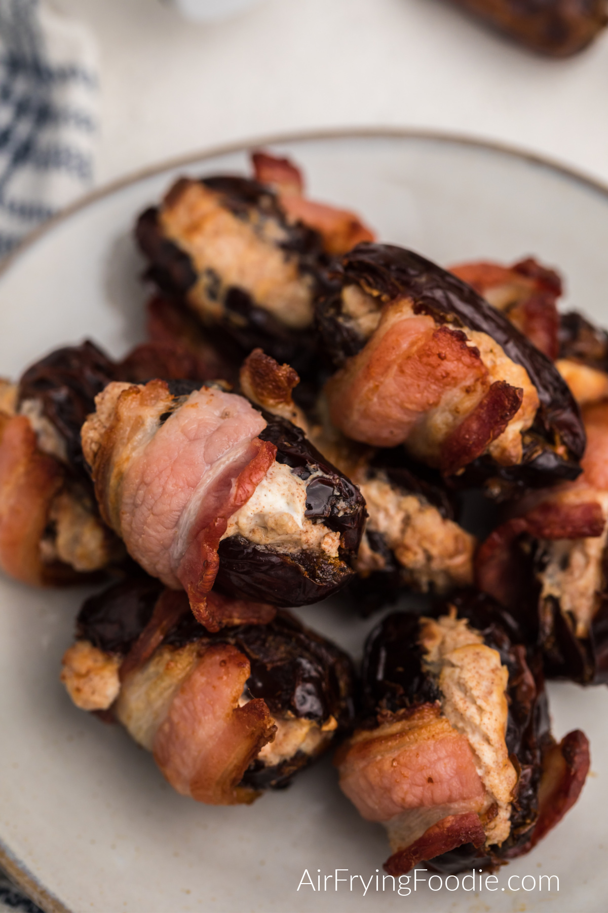 Cream cheese stuffed air fryer bacon wrapped dates in a white plate, ready to serve.