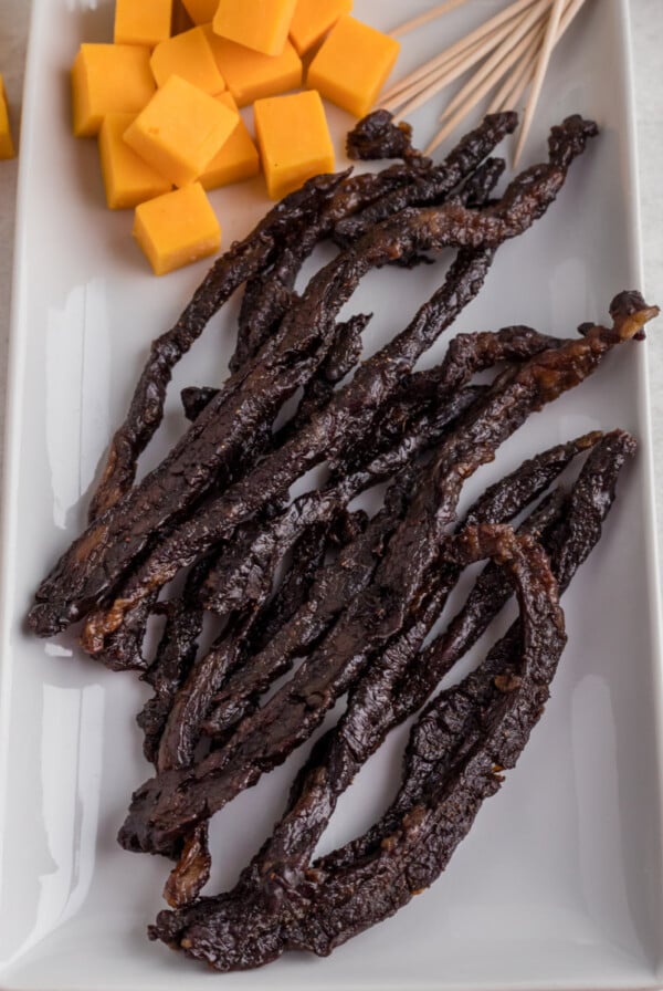 Air fryer jerky on a white plate with blocks of cheese, ready to serve.