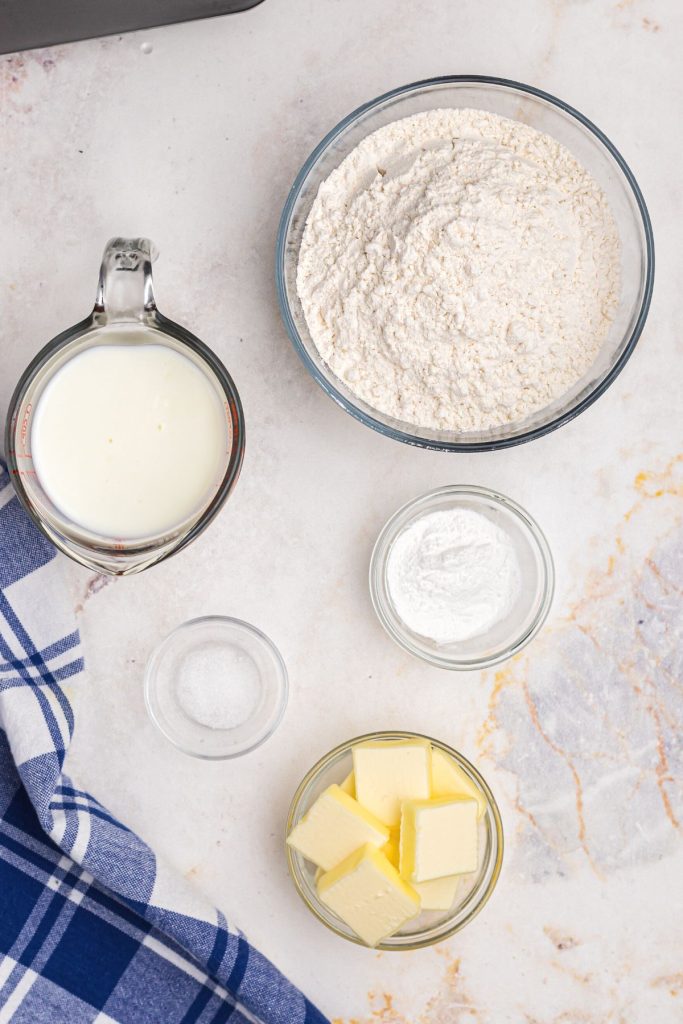 Flour, baking powder, butter, salt, and buttermilk, measured on a marble board. 