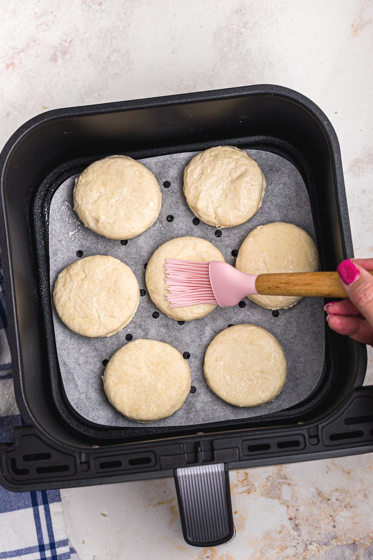 Uncooked biscuits in the air fryer basket being brushed with a milk wash.