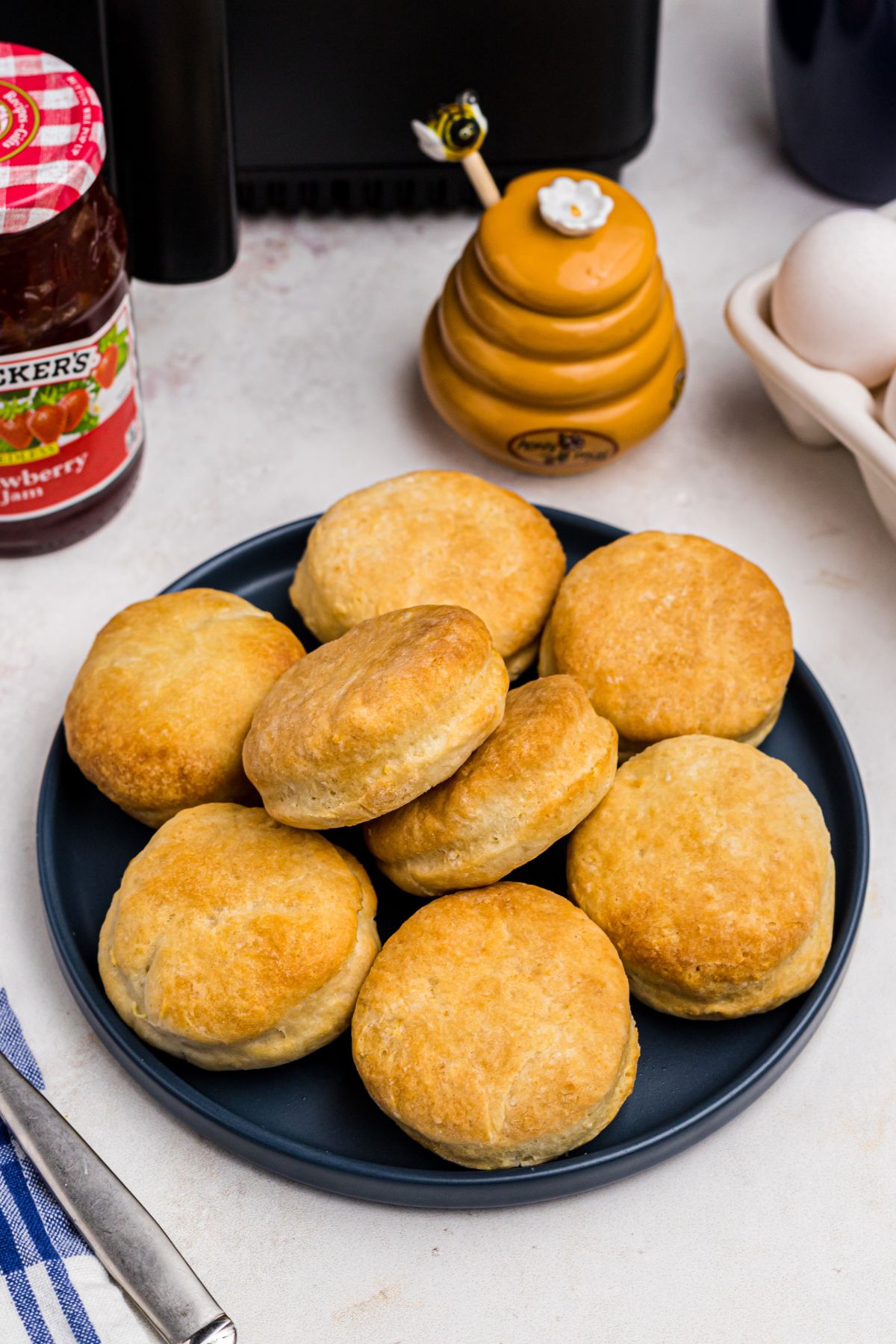 Golden air fryer biscuits stacked on a blue plate in front of jam and honey