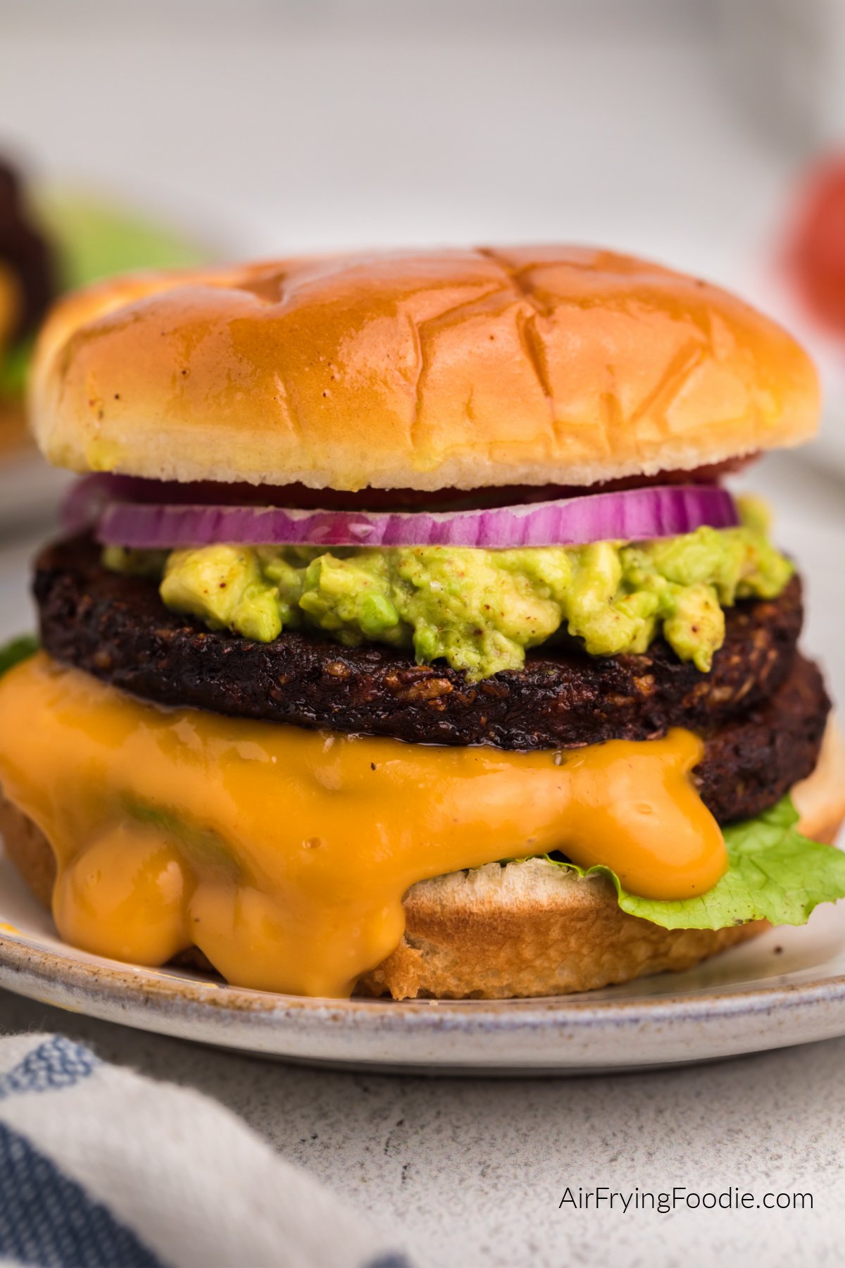 Air fried black bean burger with mashed avocado, sauce, lettuce, onion, and tomato on a bun. 