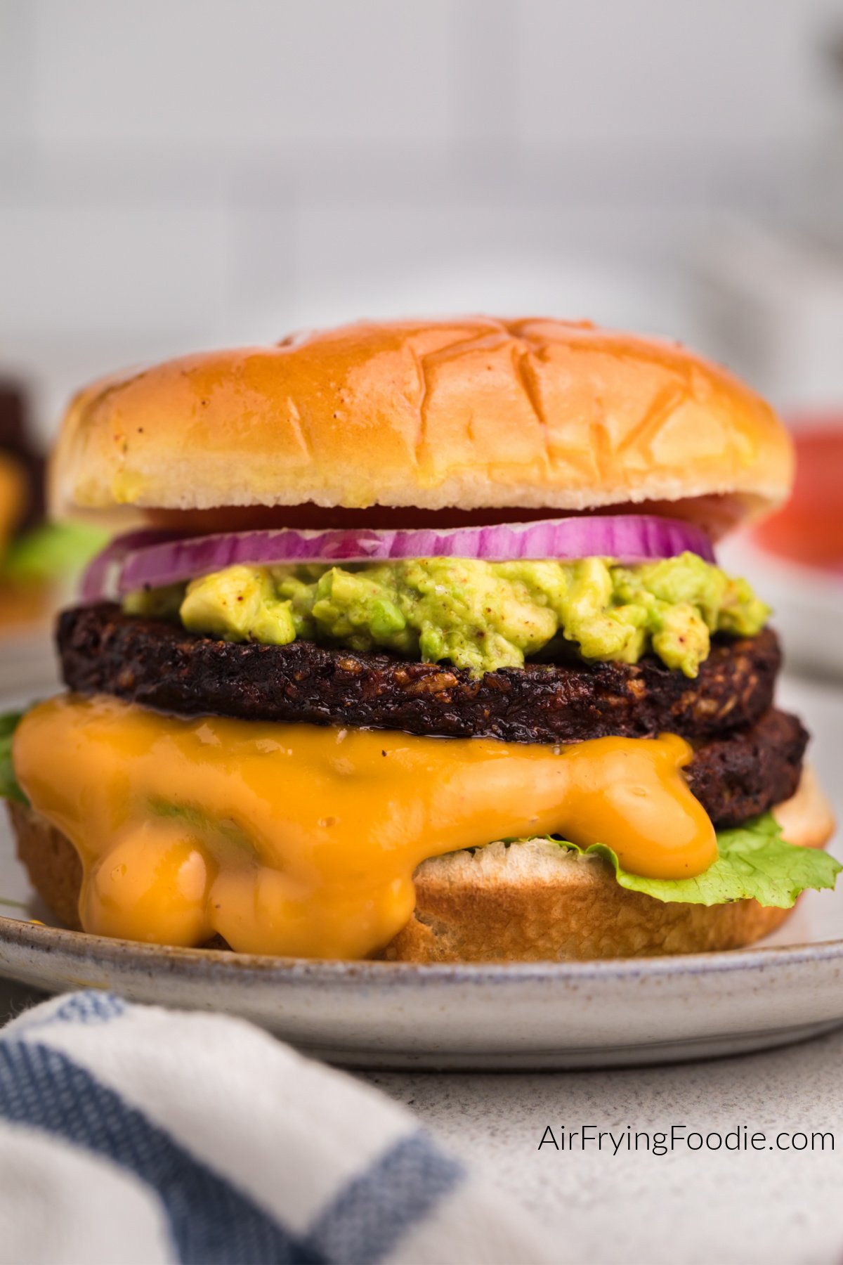 Black bean burger made in the air fryer topped with mashed avocado, onion, tomato, and sauce. 
