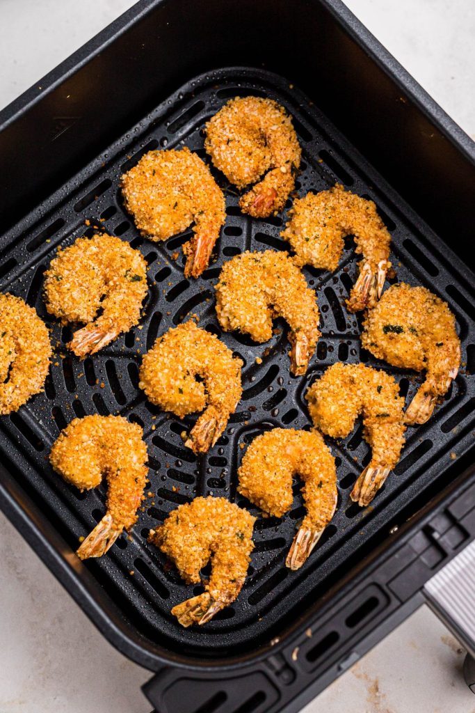Golden breaded shrimp in the air fryer basket after being cooked. 