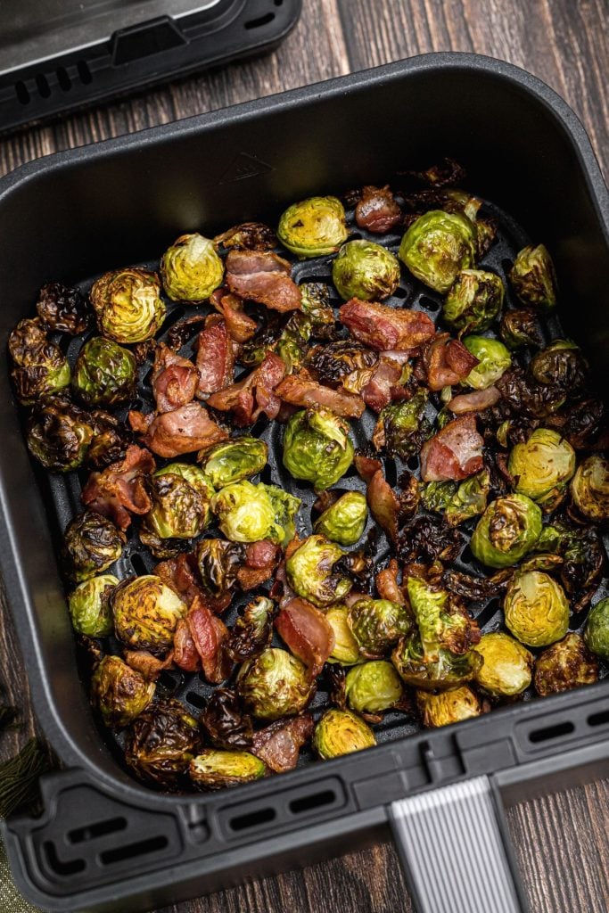 Green crispy juicy brussels sprouts with crispy bacon pieces in the air fryer basket.