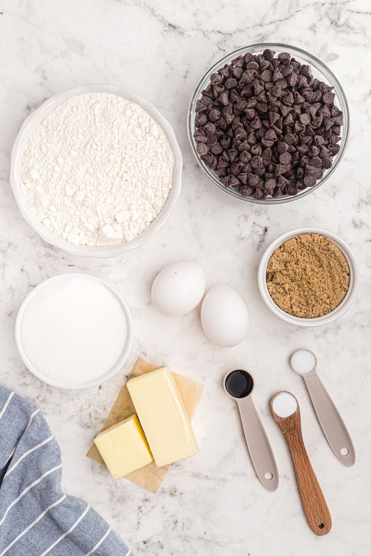 Ingredients on a marble table measured out for chocolate chip cookies. 