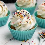 Golden cupcakes frosted and topped with sprinkles in front of the air fryer.