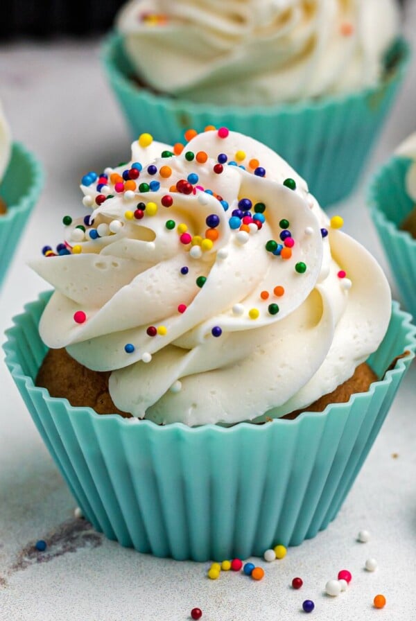 Golden cupcakes frosted and topped with sprinkles in front of the air fryer.