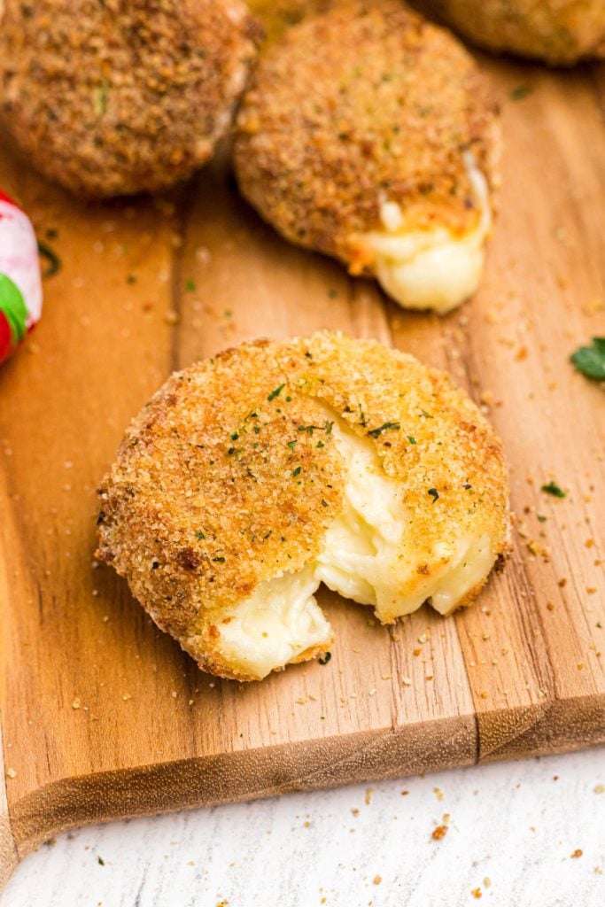 Golden fried round piece of cheese, with breading on a wooden cutting board. 