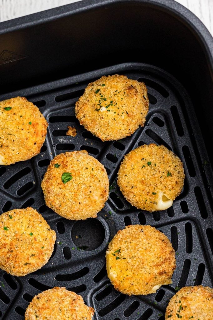 Golden breaded cheese rounds in the air fryer basket after being air friend. 