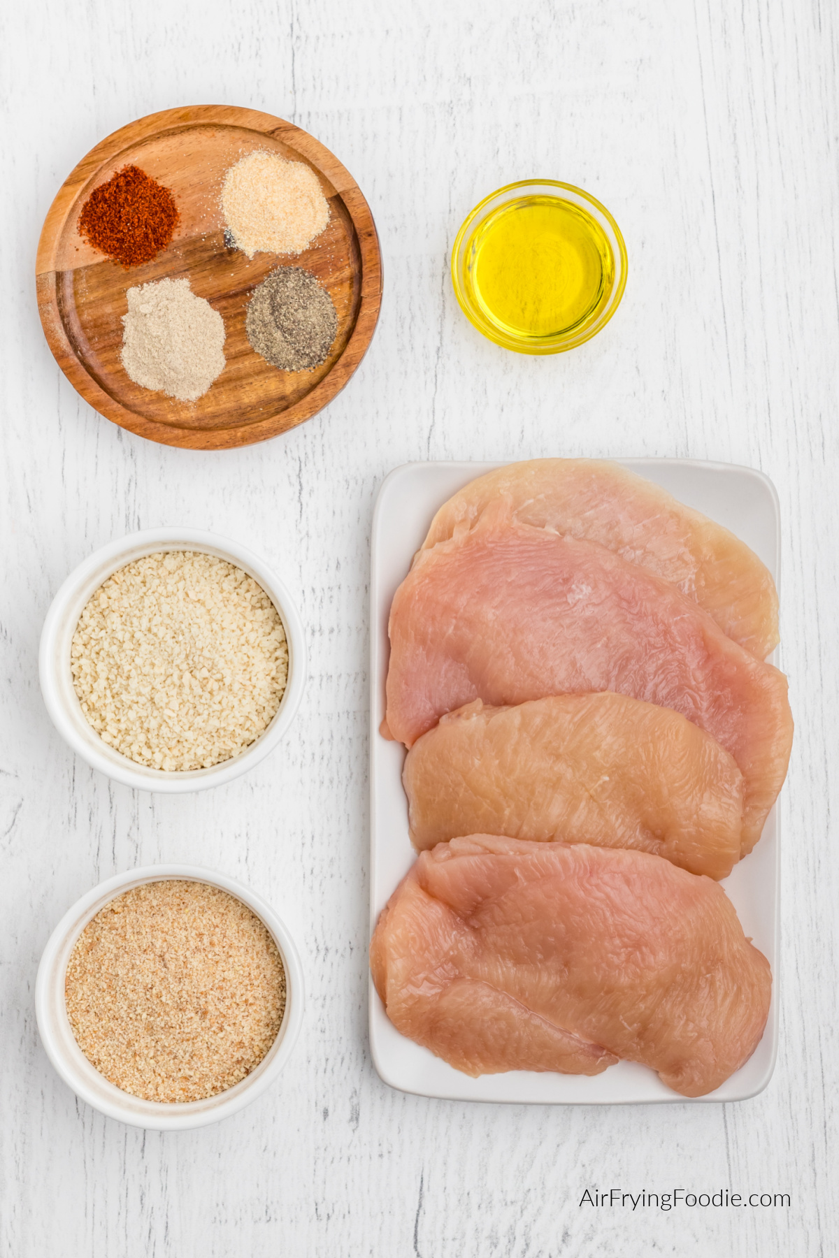 Chicken breasts, breadcrumbs, panko, seasonings, and olive oil on a table.
