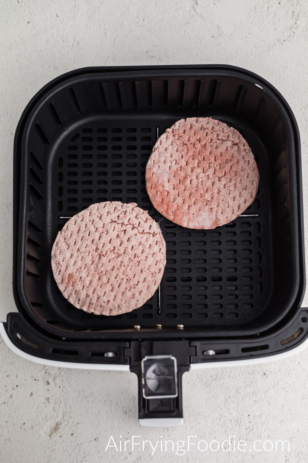 Frozen burger patties in the basket of the air fryer.