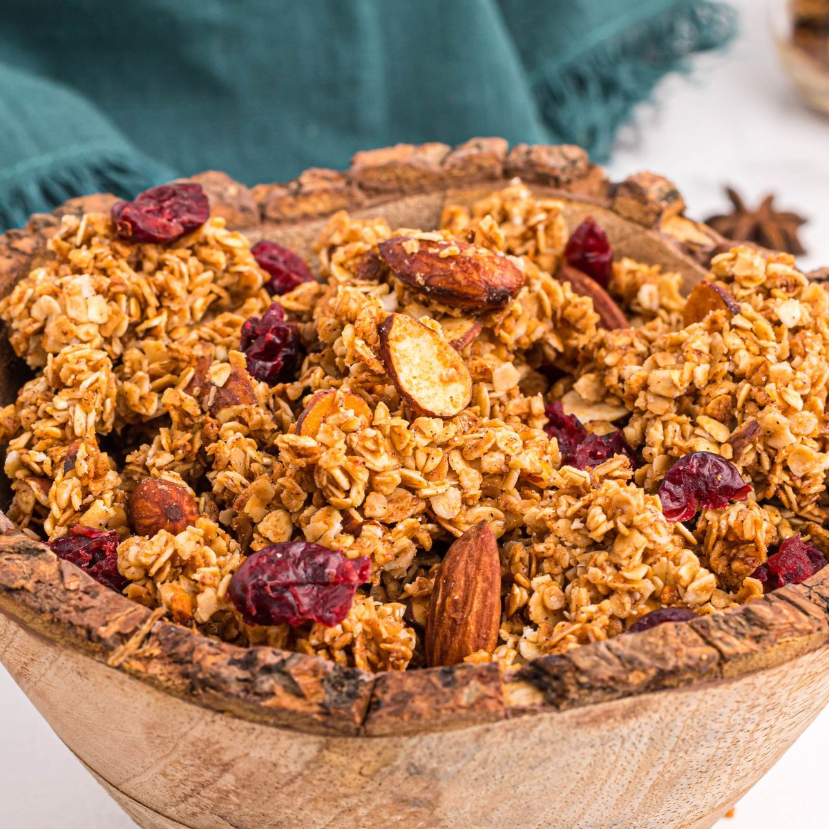 Golden granola in a wooden bowl filled with nuts and dried fruit.
