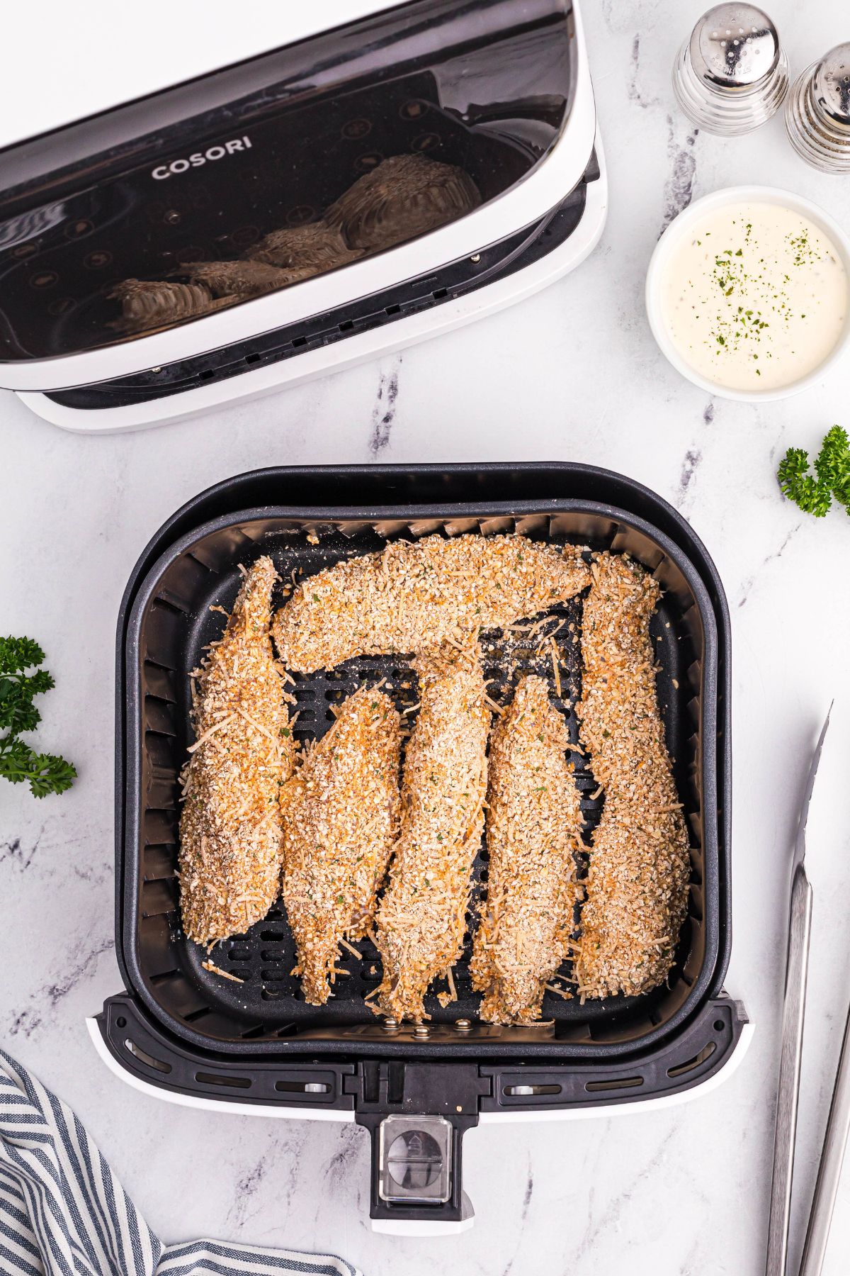 Uncooked coated chicken in an air fryer basket on a white marble table.