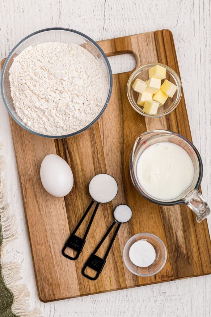 Ingredients needed to make Irish Soda Bread measured in clear glass bowls on a wooden cutting board. 