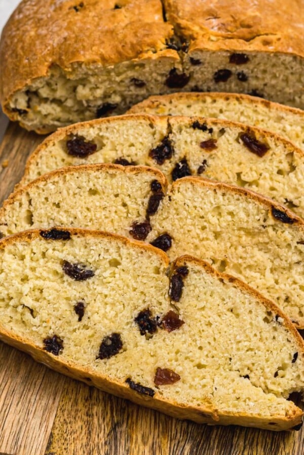 Golden Irish Soda bread filled with raisins, slices on a wooden cutting board.