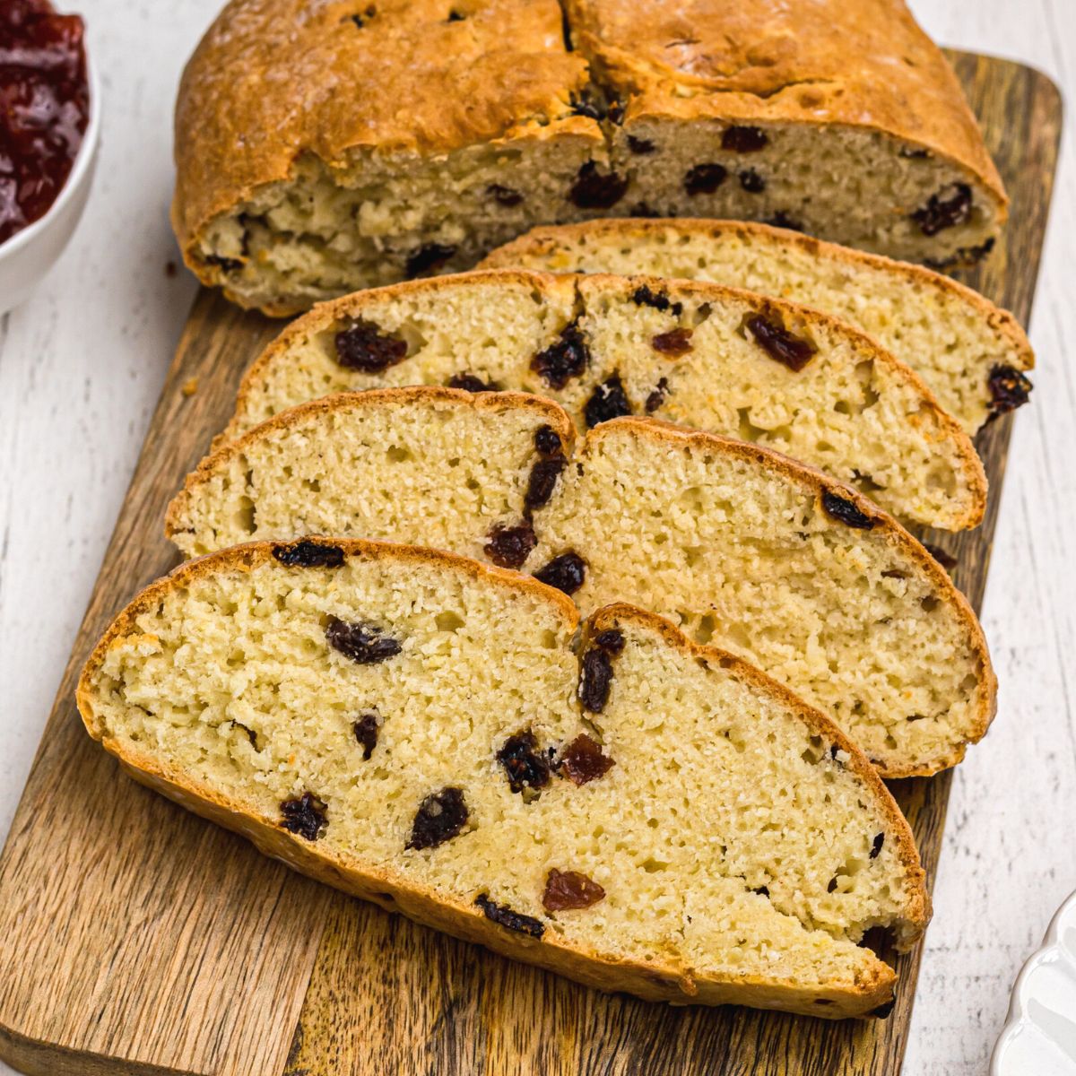 Golden Irish Soda bread filled with raisins, slices on a wooden cutting board.