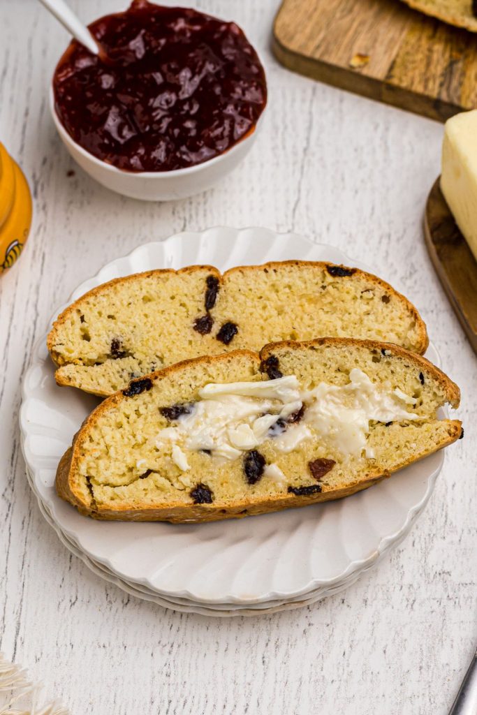 Golden slices of Irish Soda Bread with raisins, lightly buttered on a small white plate. 