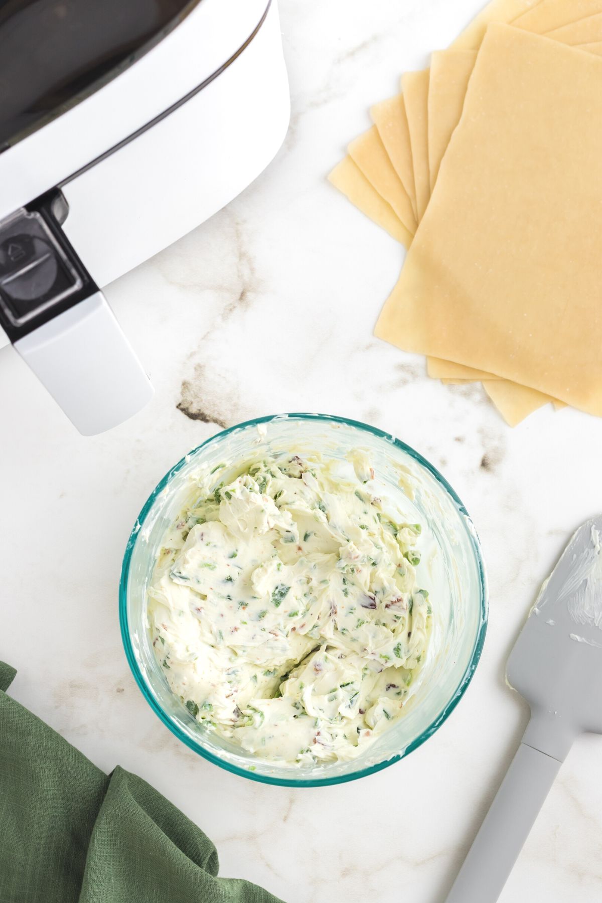 Cream cheese and chopped jalapenos mixed together in a clear glass bowl.