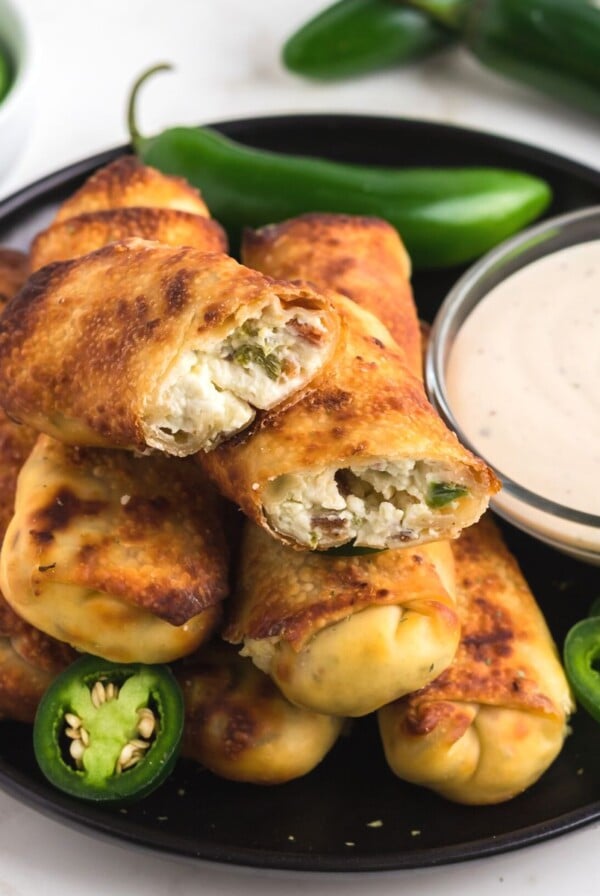 Golden egg rolls filled with cream cheese and chopped jalapenos on a black plate