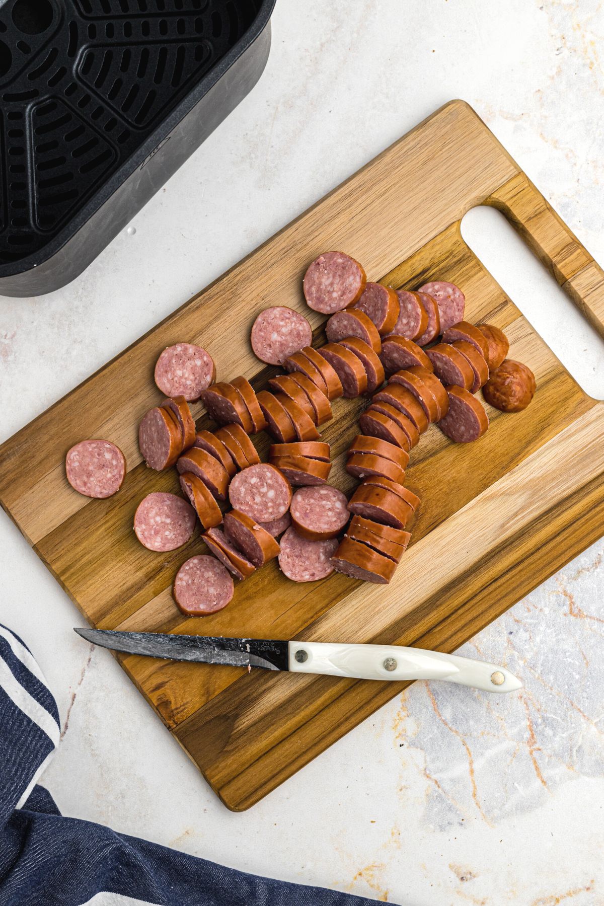 Kielbasa sliced on a wooden cutting board in front of the air fryer basket.