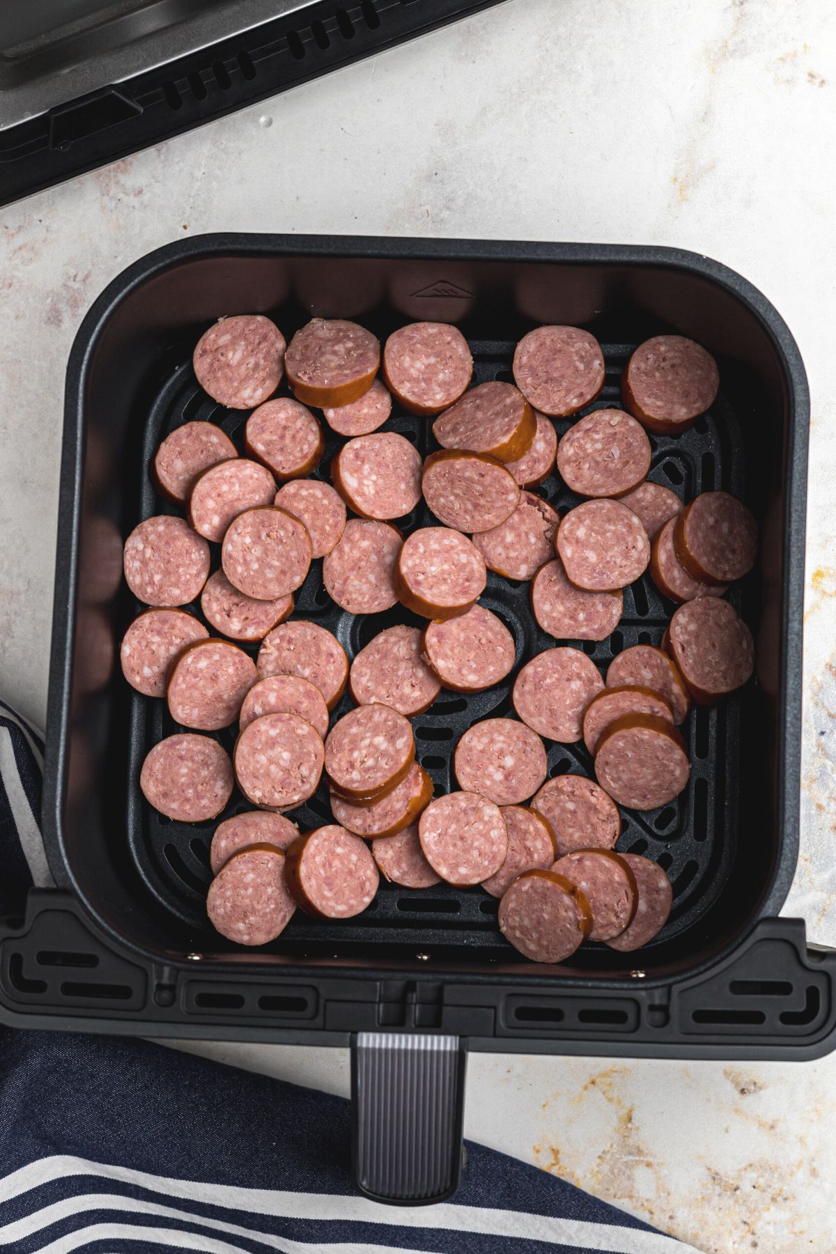 Kielbasa cut into slices in the air fryer basket before being cooked