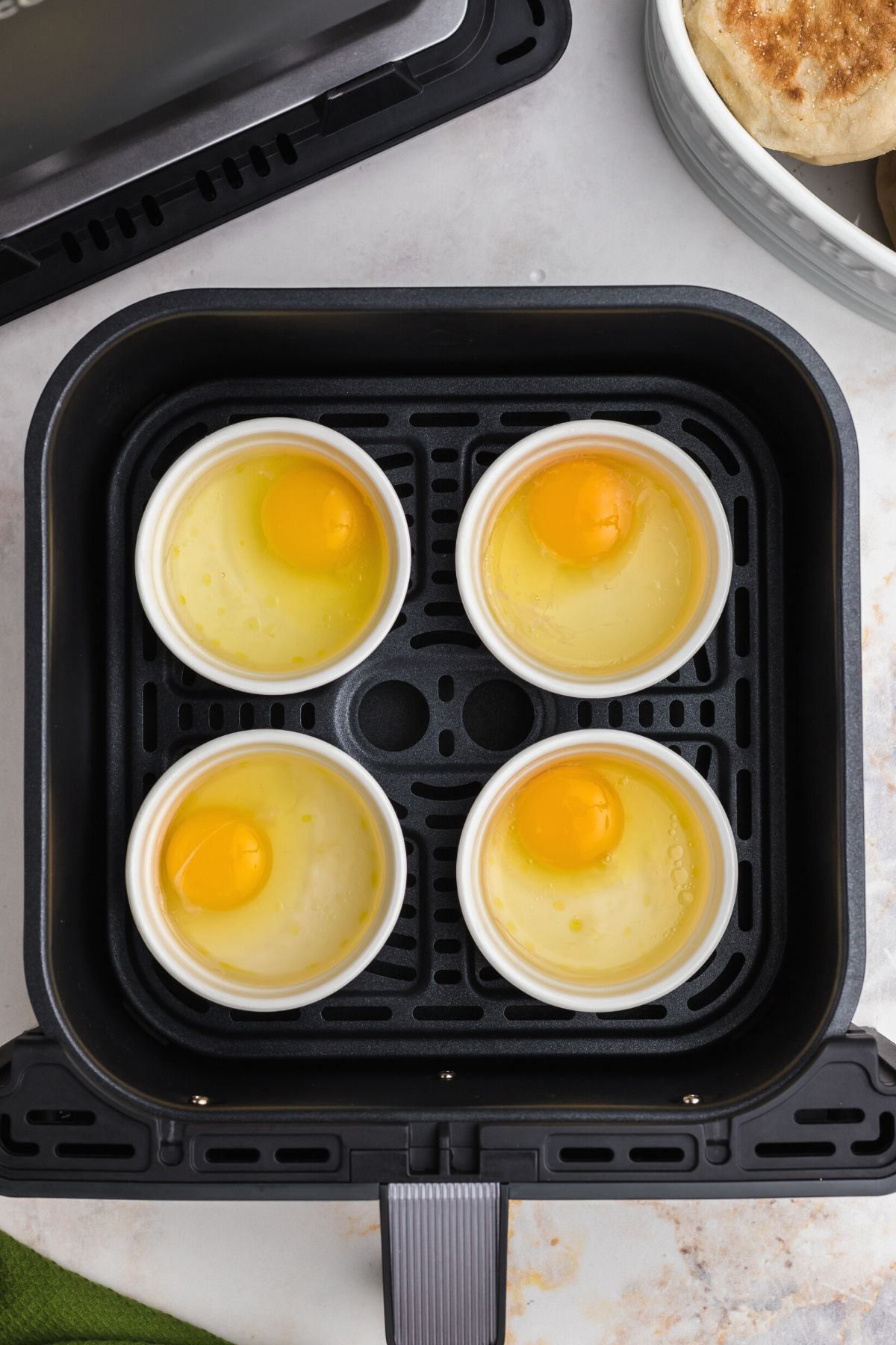 Uncooked eggs in ramekins filled with water in the air fryer basket.