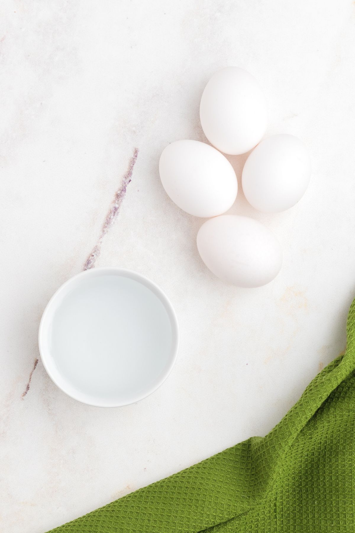 Four eggs and a ramekin of water on the marble table.