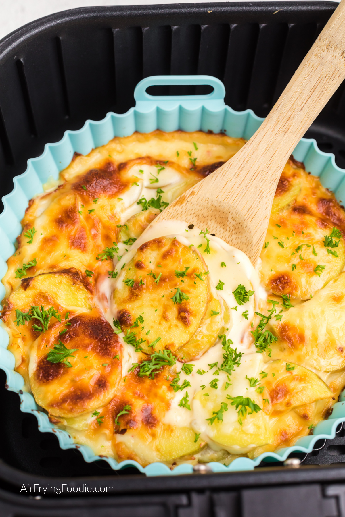 Air fryer scalloped potatoes topped with fresh parsley and a wooden spoon scooping out a serving.