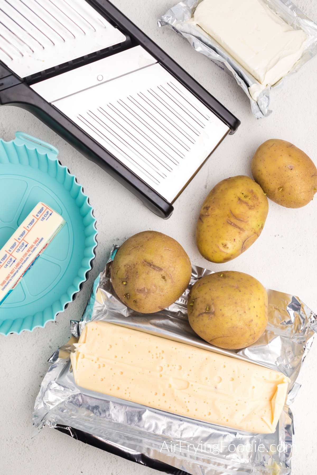 Mandolin, silicone baking dish, cream cheese, butter, queso block cheese, and potatoes.
