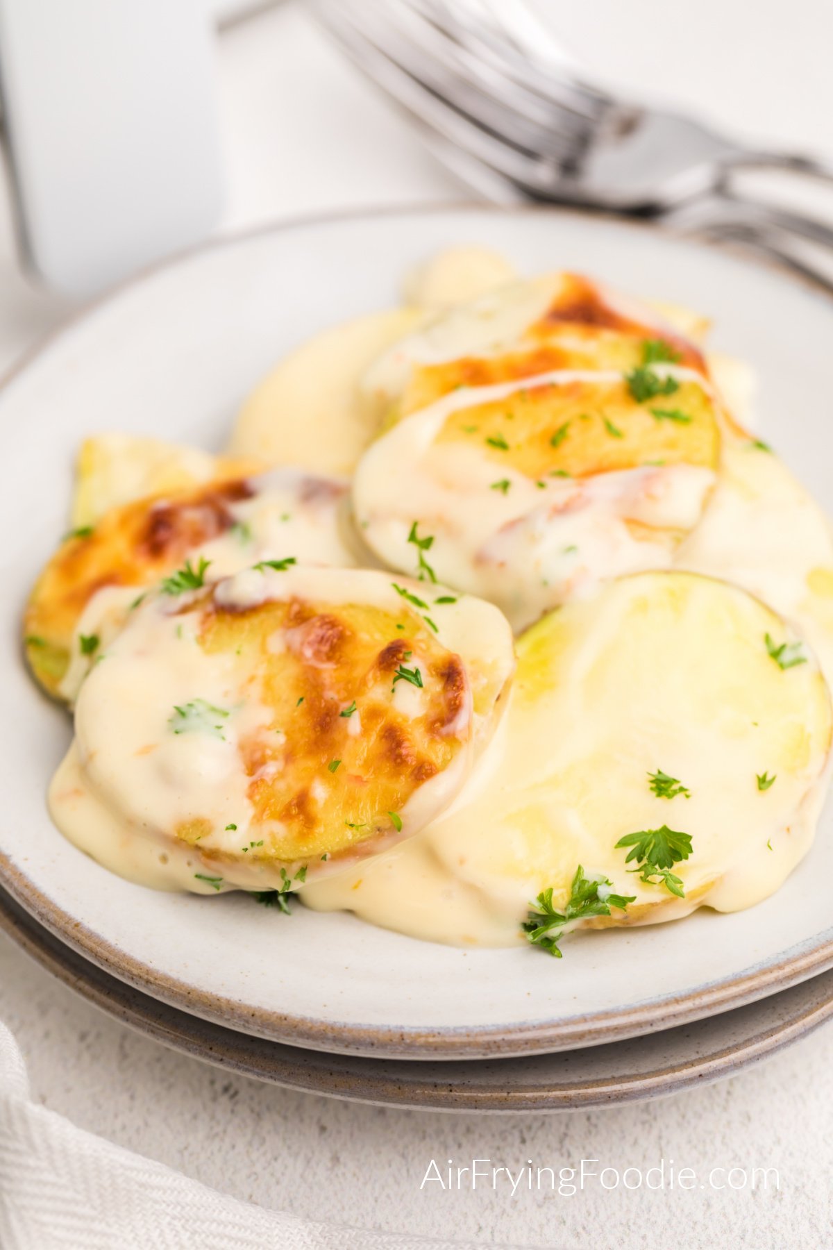 Air fried scalloped potatoes served on a plate and topped with fresh parsley.