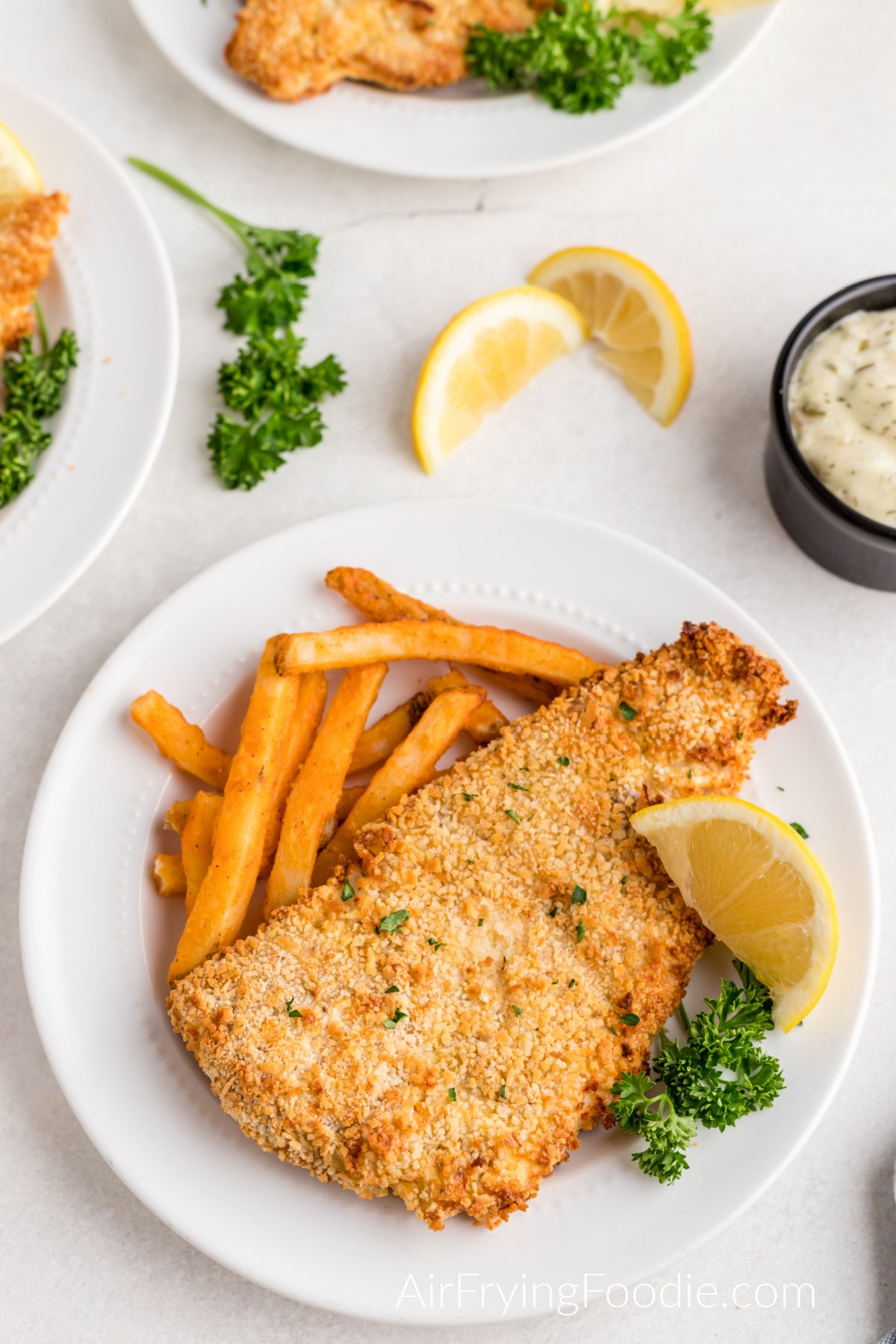 Air fryer fish served on a plate with a side of fries and lemon wedge.