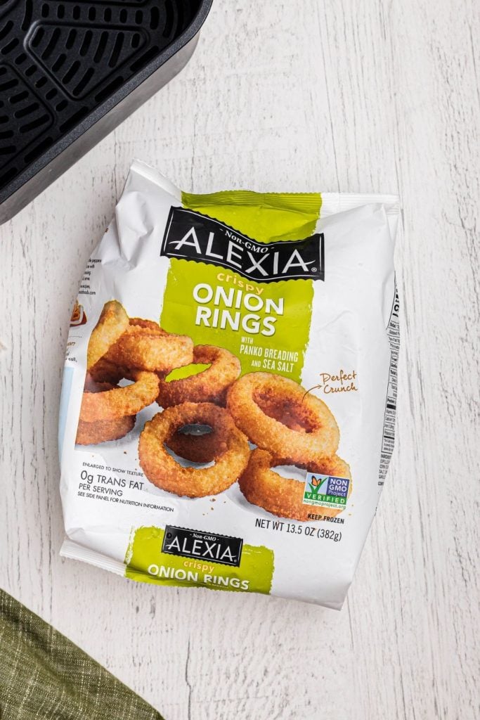 One bag of alexia crispy onion rings on a white wooden table with an air fryer basket. 