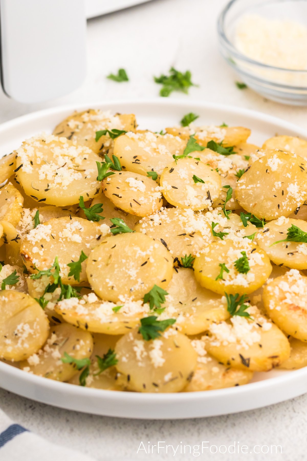 Air fried sliced potatoes on a plate with fresh parmesan and fresh chopped parsley.
